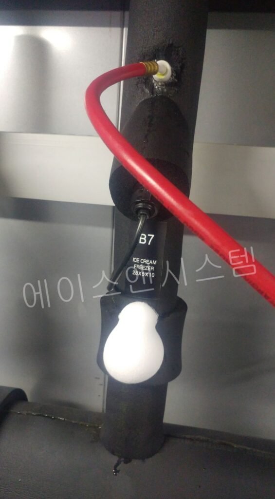 단열재로 싸인 냉동 배관에 압력 게이지 호스를 연결한 모습