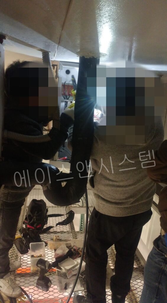 조도가 낮은 냉동창고 내부에서 랜턴을 비추며 2인 1조로 안전하게 증발기 배선을 수리 중인 에이스앤시스템 엔지니어들